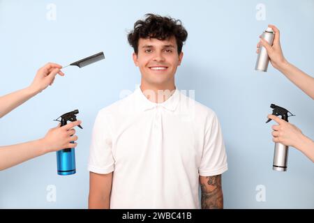 Beau jeune homme et mains féminines avec des bouteilles de spray pour cheveux sur fond bleu Banque D'Images