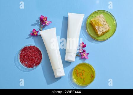 Contexte pour la présentation des produits cosmétiques extraits du safran. Deux bouteilles en plastique sans marque décorées avec des ingrédients frais sur le dos bleu Banque D'Images