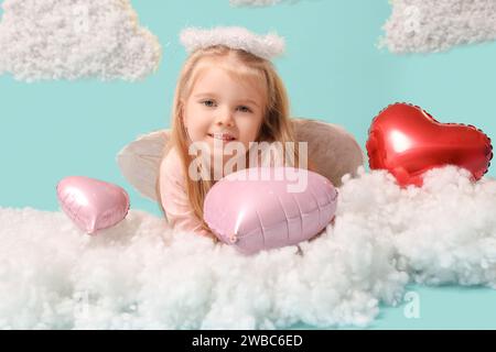 Jolie petite fille habillée comme cupidon avec des ballons en forme de cœur et des nuages sur fond bleu. Fête de la Saint-Valentin Banque D'Images