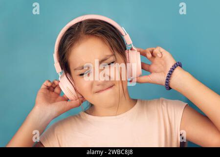 Portrait photo de belle fille avec les yeux fermés gardant smartphone écoutant de la musique avec des écouteurs roses dansant. fond bleu Banque D'Images