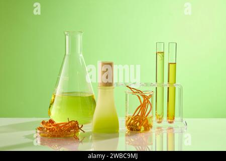 Sur le fond vert, des équipements de laboratoire contenant du cordyceps et de l'essence décorés d'une bouteille de maquette sans marque. Vue avant. Scène pour la publicité c Banque D'Images