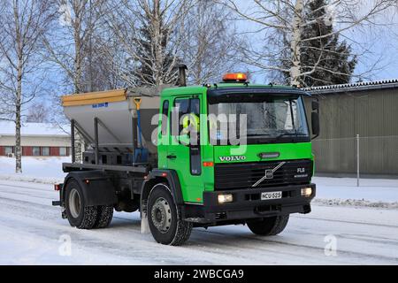 Camion vert citron Volvo FL6 grinçant épandage de gravier sur route glacée et enneigée par une journée froide de l'hiver. Salo, Finlande. 27 décembre 2023. Banque D'Images