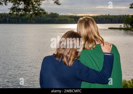 Le dos de deux sœurs debout l'une à côté de l'autre regardant un lac Banque D'Images