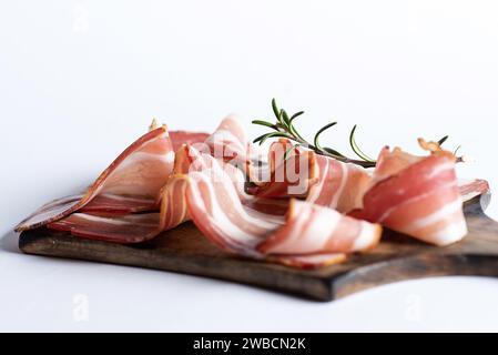 Rouleaux de bacon fumé sur une planche à découper en bois et un fond blanc Banque D'Images