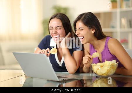 Deux amis joyeux qui regardent les médias rire et manger des chips à la maison Banque D'Images