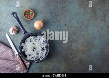 Une poêle avec des oignons hachés debout sur une serviette en lin sur une surface sombre. Banque D'Images