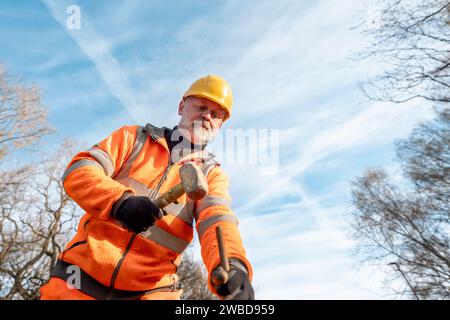 Le constructeur défonce la route en posant des goupilles en acier avec un marteau en morceaux pendant les travaux routiers. Constructeur martelant des barres d'acier dans l'asphalte pendant le roadwor Banque D'Images