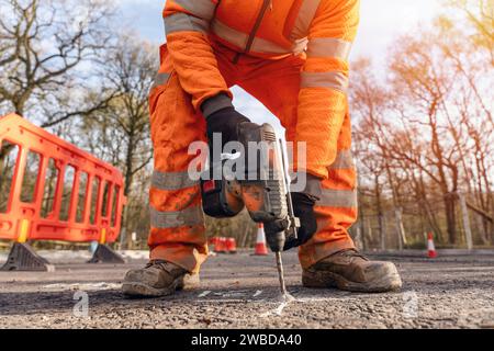 Gros plan d'un constructeur utilisant une perceuse à percussion sans fil pour percer des trous dans la route à l'emplacement marqué par l'arpenteur du technicien de chantier Banque D'Images