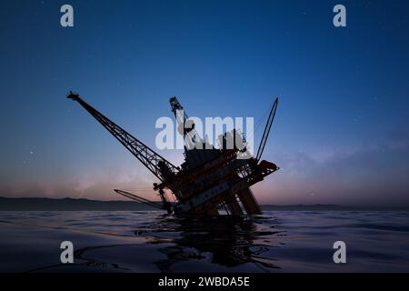 Vue captivante d'une plate-forme pétrolière offshore qui se détache d'un ciel étoilé au crépuscule, avec des reflets sereins dansant sur l'environnement Banque D'Images