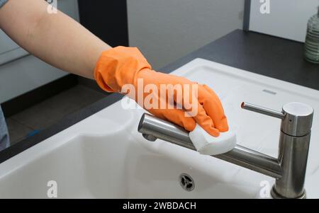 Gros plan de la main de la femme dans le gant orange nettoyant évier de cuisine Banque D'Images