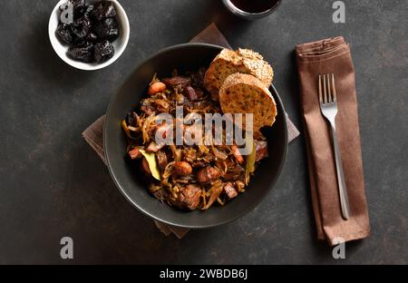 Vernis traditionnel Bigos dans un bol en céramique noire sur fond de pierre sombre. Ragoût de chou avec choucroute, champignons, viandes fumées et épices. Top vie Banque D'Images