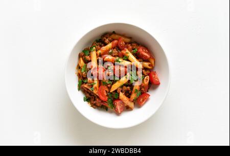 Bol de pâtes de penne à la bolognaise avec de la viande hachée, des tomates et des légumes verts sur fond blanc. Vue de dessus, pose à plat Banque D'Images