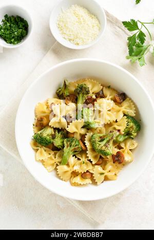 Pâtes Farfalle avec brocoli rôti et champignons dans un bol en céramique blanche sur fond clair. Plat préparé maison de pâtes farfalle avec rôti Banque D'Images