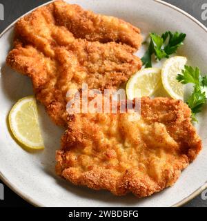 Vue rapprochée de wiener schnitzel avec citron et feuilles de persil sur plaque blanche. Banque D'Images