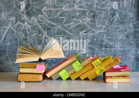 Concept d'éducation et de lecture avec un groupe de livres colorés et de notes adhésives, un livre ouvert sur fond de tableau noir Banque D'Images