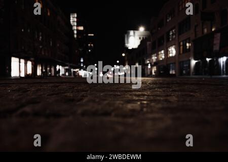 Une photo nocturne atmosphérique d'une rue urbaine avec des panneaux lumineux, des bâtiments et des lampadaires Banque D'Images