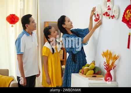 Joyeuse famille accrochant des décorations de Tet faites à la main sur le mur Banque D'Images