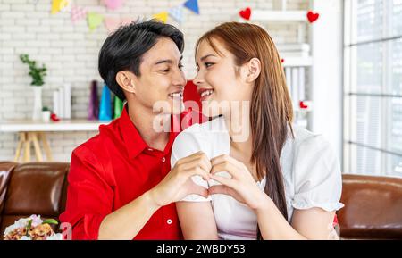 Amour, heureux et main coeur par couple sur le canapé avec amour, soin et confiance à la maison ensemble. Emoji, forme et homme avec les mains de la femme pour soutenir l'espoir Banque D'Images