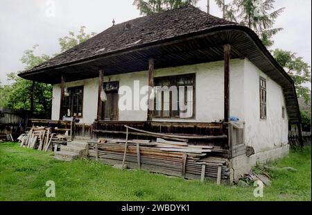 Comté de Vrancea, Roumanie, env. 1995. Une maison traditionnelle avec toit en bois en mauvais état. Bois empilé dans la cour. Banque D'Images