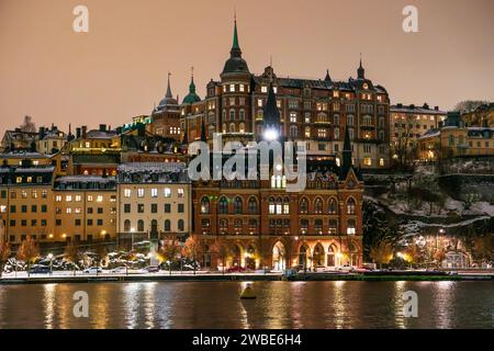 Stockholm, quartier de Sodermalm la nuit en hiver avec neige sur le sol, bâtiments historiques. Ciel nuageux, reflets de lac. Banque D'Images