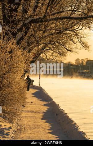 Une vue sur un sentier en hiver sur l'île de Skeppsholmen, Stockholm, avec de la fumée de mer visible du vent froid. Une femme marchant sous le soleil d'hiver. Banque D'Images