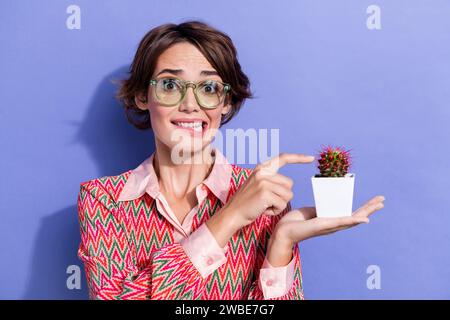 Photo portrait de jolie jeune fille toucher nerveux cactus épine porter tenue d'impression tendance isolé sur fond de couleur violette Banque D'Images