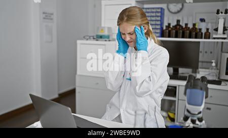 Stressé jeune femme scientifique en blouse de laboratoire avec mal de tête en laboratoire Banque D'Images