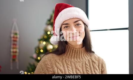 Jeune belle femme hispanique portant un chapeau de noël debout à la maison Banque D'Images