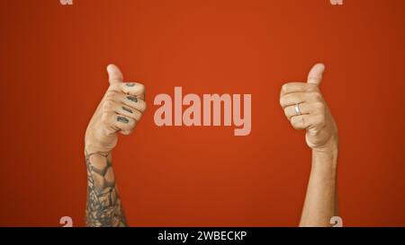 Pouces levés ! les mains tatouées de l'homme approuvent avec un geste pouce levé sur un fond rouge vif isolé, signalant un signe cool 'ok'. Banque D'Images