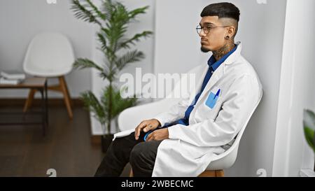 Jeune médecin latin épuisé en manteau blanc, assis stressé dans la salle d'attente de la clinique, son beau portrait gravé de concentration Banque D'Images