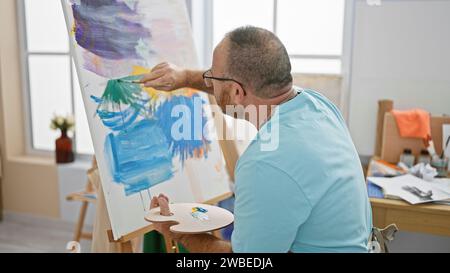 Bel homme caucasien d'âge moyen, un artiste profondément concentré alors qu'il dessine passionnément un portrait dans son atelier d'art intérieur Banque D'Images