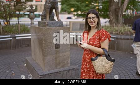 Incroyablement belle femme hispanique dans des lunettes, debout près de la statue emblématique hachiko sur la rue animée de tokyo, capturant l'expression urbaine japonaise de Banque D'Images