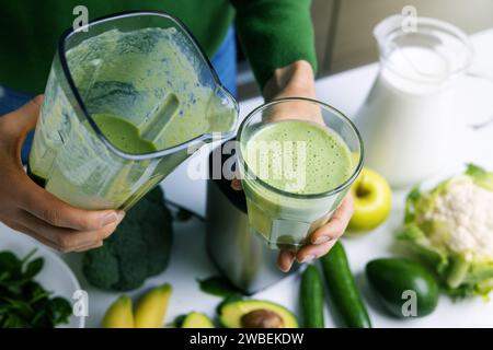 femme versant un smoothie vert frais maison dans un verre à base de légumes et de fruits. mode de vie sain Banque D'Images