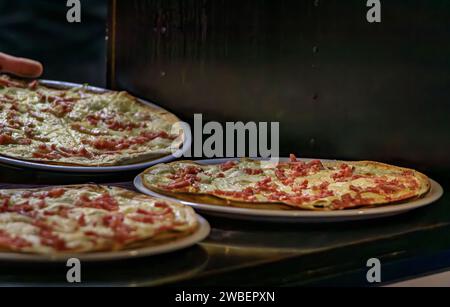 Chef passant flammekueche ou tarte flambee avec du fromage et du bacon à travers une fenêtre de service dans un restaurant, Colmar, France, village de la route des vins d'Alsace Banque D'Images