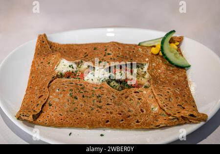 Spécialité française, crêpe de sarrasin avec cuisses de grenouille, tomates et fromage dans un restaurant winstub à Colmar, en France, village de la route des vins d'Alsace Banque D'Images