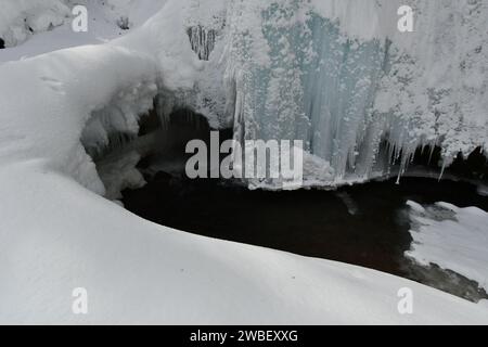 Une scène hivernale idyllique avec une cascade de glace sereine en cascade sur des rochers et des sculptures de neige en arrière-plan Banque D'Images