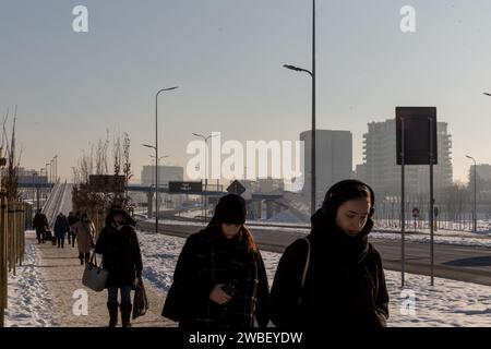 Cracovie, Pologne, 10 janvier 2024. Les navetteurs marchent sur un trottoir dans le nord de Cracovie alors que la brume de pollution de l'air est vue au-dessus de la ville alors que les températures ont chuté bien en dessous de 0 degrés Celsius. La pollution atmosphérique a été déclarée très malsaine et la concentration de PM2,5 était 30 fois plus élevée que les lignes directrices annuelles DE L'OMS sur la qualité de l'air. La pollution est une combinaison de manque de vent et de basses températures qui ont forcé la ville et ses habitants à chauffer leurs maisons. Banque D'Images