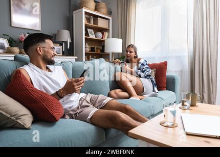 Concept d'ennui. Jeune couple utilisant des smartphones, assis sur le canapé à la maison, ne sait pas quoi faire les jours de week-end tout est ennuyeux. Banque D'Images