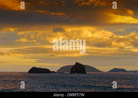 Vue sur la mer des rochers Ilheu em PE et Ilheu Deitado sous un ciel nocturne ambre avec nuages, Madalena, Pico, Açores, Portugal Banque D'Images