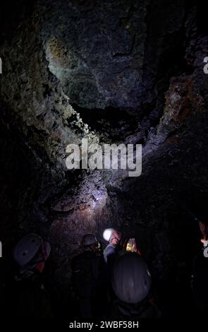 Explorateurs de grottes dans le tunnel de lave Gruta das Torres avec des casques regardant une paroi rocheuse illuminée dans l'obscurité, Gruta das Torres, île de Pico Banque D'Images