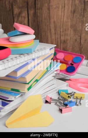 Beaucoup de livres différents, avion en papier et papeterie scolaire sur la table blanche. Retour à l'école Banque D'Images