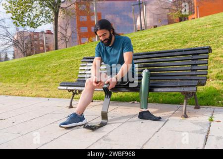 Homme handicapé physique ajustant la jambe prothétique avant de courir assis sur un banc de parc urbain Banque D'Images