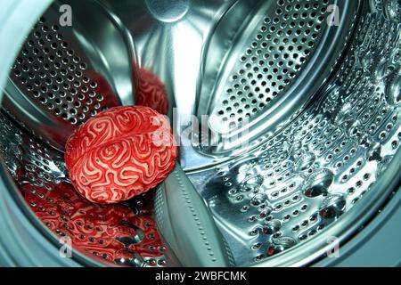 Cerveau humain en caoutchouc rouge à l'intérieur d'une machine à laver, concept de lavage de cerveau. Banque D'Images