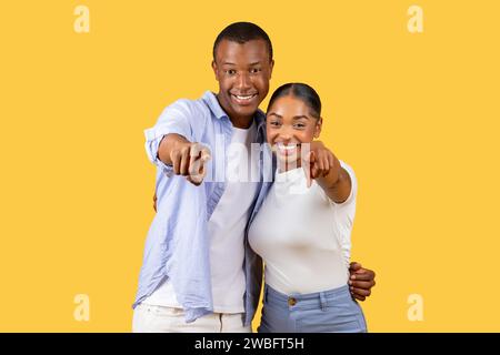 Couple noir pointant vers la caméra, amical et invitant, fond jaune Banque D'Images