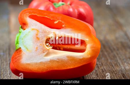 Poivrons rouges entiers naturels et frais, un coupé en deux sur une planche de bois. Banque D'Images