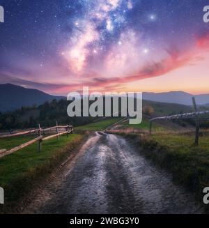 Voie lactée sur la route rurale, clôture en bois dans les montagnes la nuit Banque D'Images