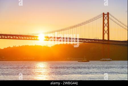 Lever de soleil doré derrière le pont 25 de Abril à Lisbonne, Portugal, projetant une lueur chaude sur le Tage dans un moment de paix et de beauté. Banque D'Images