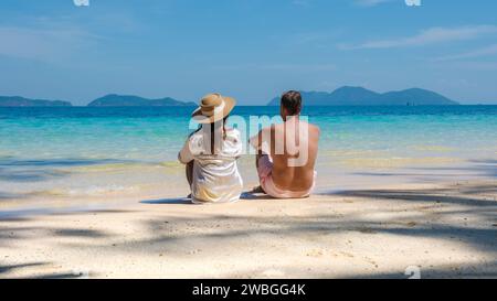 Un jeune couple d’hommes et de femmes assis sur une plage tropicale lors de vacances de luxe en Thaïlande, couple diversifié allongé sur la plage de Koh Wai I. Banque D'Images