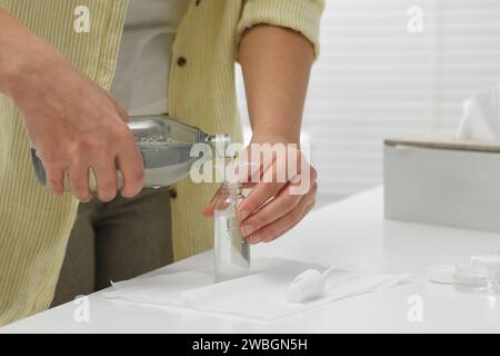 Femme versant le produit cosmétique dans la bouteille en plastique au comptoir blanc dans la salle de bain, closeup. Accessoires de bain Banque D'Images