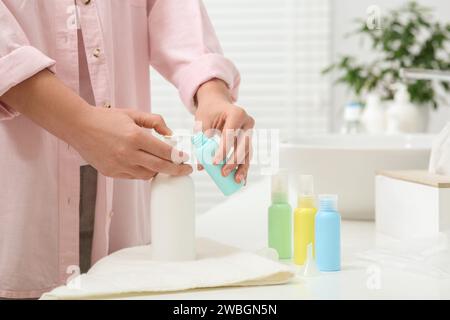 Femme versant le produit cosmétique dans la bouteille en plastique au comptoir blanc dans la salle de bain, closeup. Accessoires de bain Banque D'Images